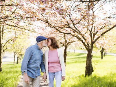 Beautiful senior couple in love on a walk outside, enjoying spring nature under blossoming trees. Man and woman kissing.